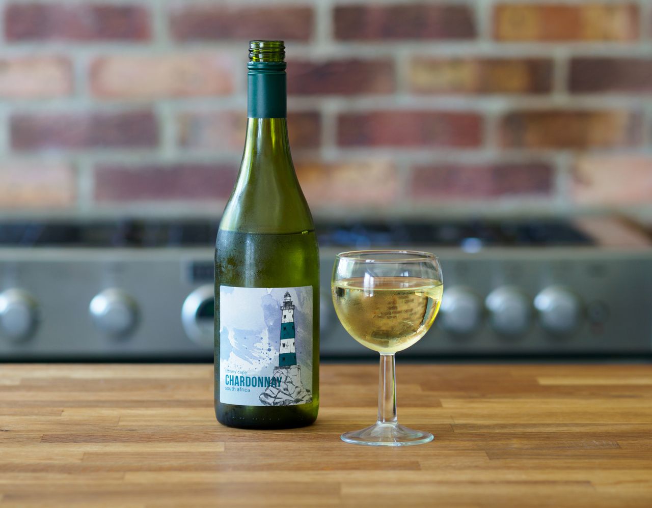 about-img Close-up of a Chardonnay wine bottle and glass on a wooden table with a brick background.
